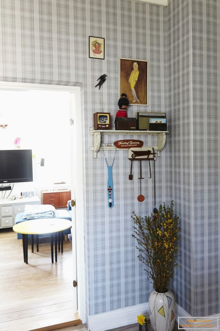 Chodba s kockou tapetou, podlahová váza pod stenou, vedľa otvorených dverí do obývacej izby