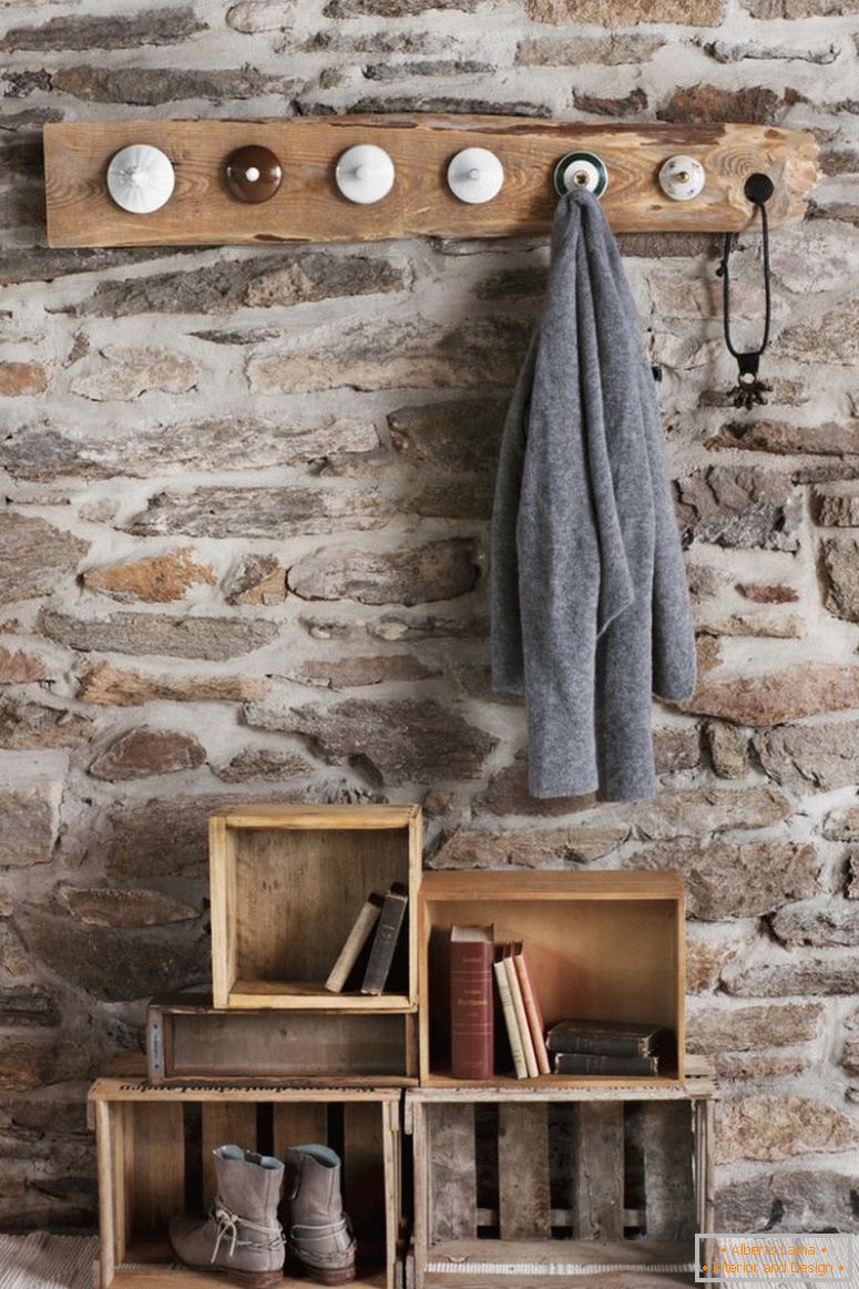 Rustikálna DIY šatňa v miestnosti s kamennou stenou; kožušinové kolíky vyrobené zo starých porcelánu z porcelánu a starých drevených prepraviek na podlahe ako skladovanie