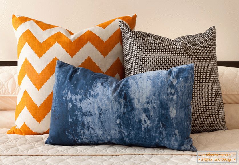 Jasné oranžové, modré a čierne a biele dekoratívne vankúše so zaujímavými výtlačkami na posteli