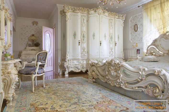 Snehovo-bielá spálňa s vyrezávaným masívnym nábytkom z dreva. Posteľ s vysokou čiapočkou na čelo, elegantne zapadá do interiéru v barokovom štýle.