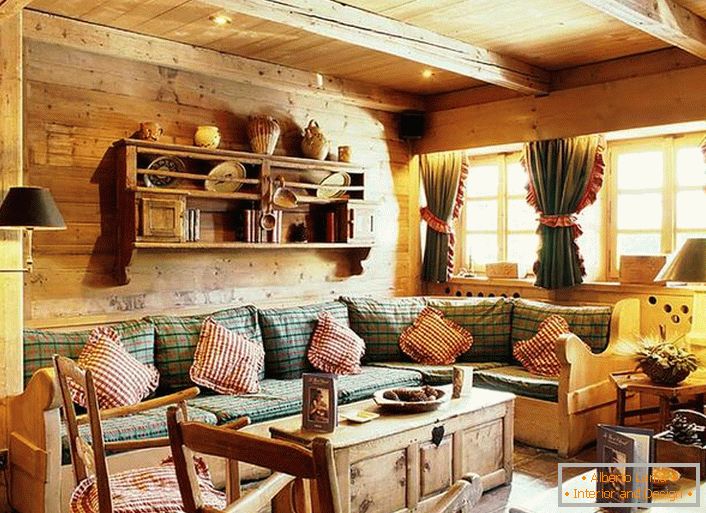Drevená dekorácia stien, kontrastné vankúše na mäkkej pohovke, husté závesy s volánkami na oknách. Útulná obývacia izba v rustikálnom štýle vo vidieckom dome.